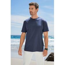 Dunkelblau Mann in dunkelblauem T-Shirt steht am Strand mit Blick zur Kamera.