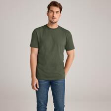 Khaki Mann in olivgrünem T-Shirt mit Jeans, stehend vor neutralem Hintergrund.