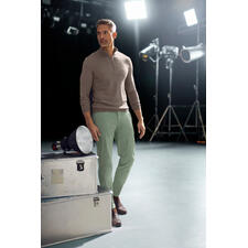 Avocado Mann trägt Chinos und steht in einem Studio.