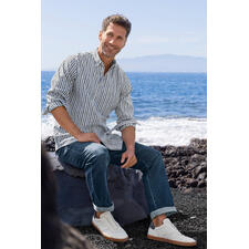 The BDO-Shirt, Limited Edition No. 76 Ein Mann sitzt auf einem Stein am Meer, trägt ein gestreiftes Hemd und leichte Schuhe.