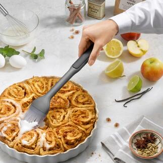 Hand mit einem Backpinsel, der einen warmen Zimtkuchen bestreicht.