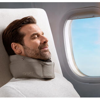 Mann mit Reisekissen entspannt am Fenster im Flugzeug.