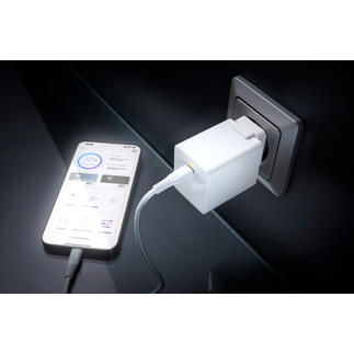 Weißer USB-Ladeadapter steckbar in eine Wandsteckdose, Smartphone angeschlossen.