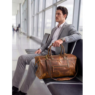 Mann sitzt am Flughafen mit Büffelleder-Weekender neben sich.