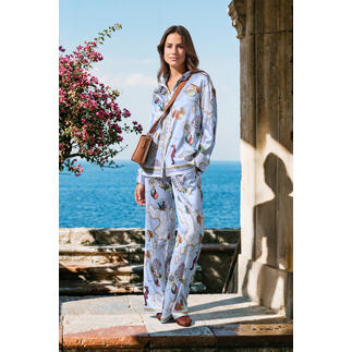 Frau in seidenem pyjama mit buntem Blumenmuster am Meer.