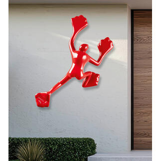 Rotere Skulptur an einer hellen Wand im Außenbereich.