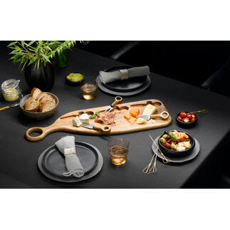 Design-Servierbrett aus Akazienholz mit Käse, Obst und Snacks auf einem dunklen Tisch.