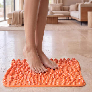 goFit-Fußreflexzonenmatte in leuchtendem Orange, auf einem hellen Fußboden mit Füßen darauf.