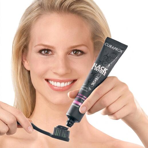 Frau hält eine Zahnbürste mit schwarzer Whitening-Zahncreme in der Hand, lächelt.