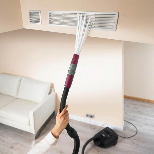 Hand mit Staubsaugeraufsatz, der eine Lüftungsschlitze reinigt.
