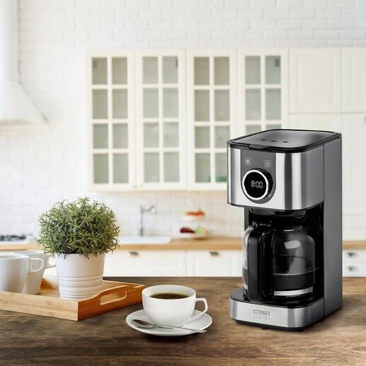 Design-Kaffeemaschine auf Tisch mit Kaffee und Pflanze.