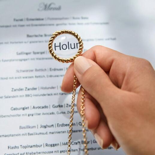 Hand hält Lupe an einer goldenen Kette über einem Menü.