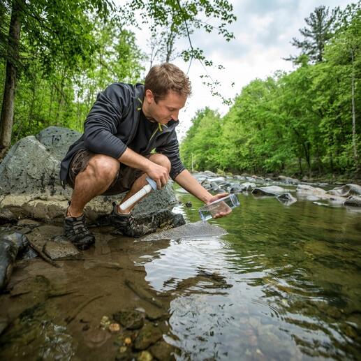 Mann füllt Wasser aus einem Bach mit einer Wasserfilter-Flasche
