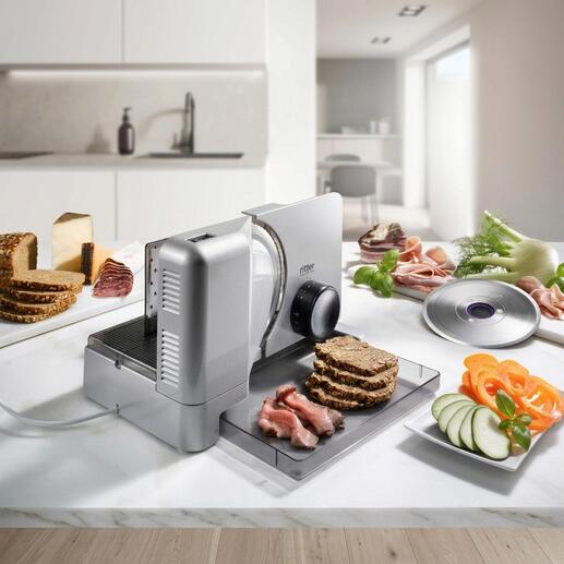 Allesschneider Duo Plus schneidet Brot und Wurst auf einer Arbeitsfläche.