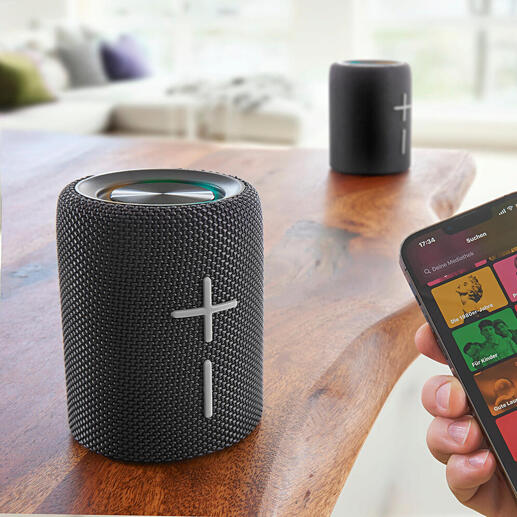 Smartphone zeigt Musik-Streaming-App neben Teilbarem Bluetooth Lautsprecher.