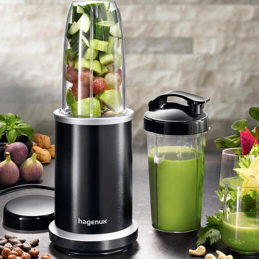 Smoothie-Blender mit Obst und Gemüse in der Schüssel und einem Becher daneben