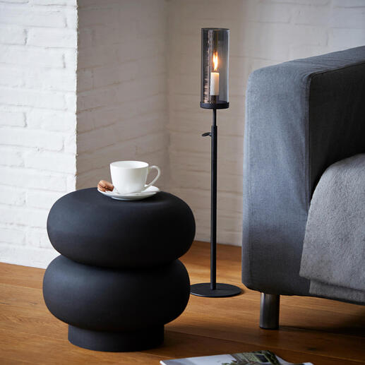 Höhenverstellbares Windlicht neben Sofa, auf schwarzem Beistelltisch mit Tasse und Zeitschrift.