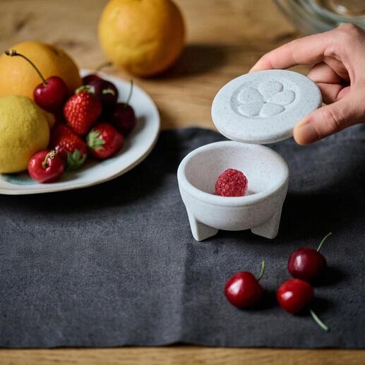 Porzellan-Fruchtfliegenfalle mit einer Hand, die den Deckel öffnet und Obst auf dem Tisch.