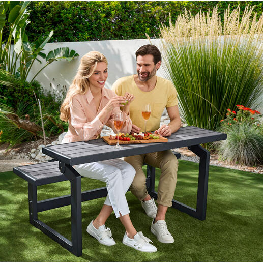 Auf Wunsch im Nu ein praktischer Essplatz. Paar sitzt an Vario-Picknicktisch im Garten und genießt Snacks und Getränke.