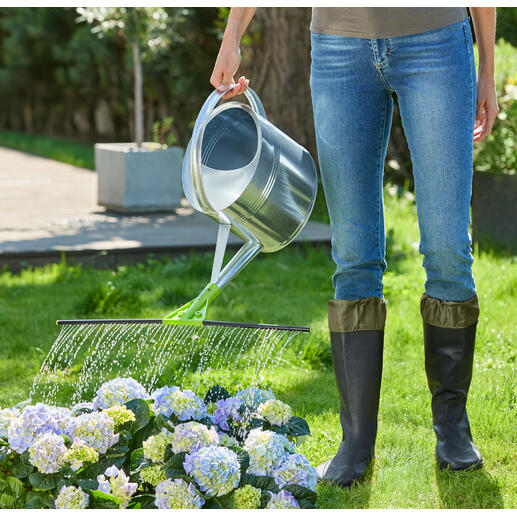 Person gießt mit einer Gießkanne Pflanzen im Garten.