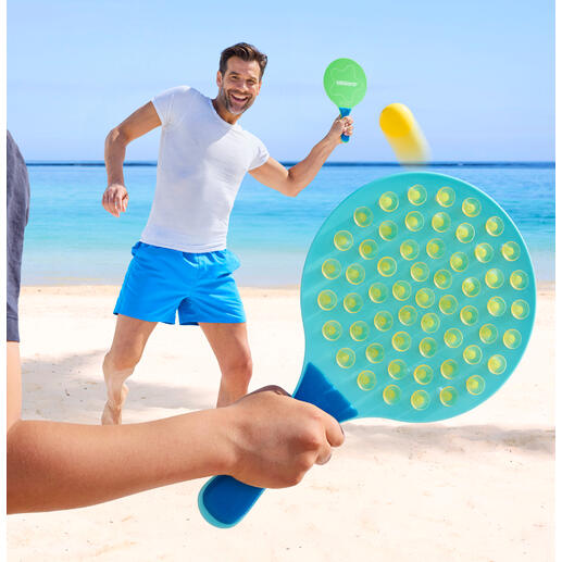 Mann spielt am Strand mit einem ovalen Schlagspiel und trifft den Ball.