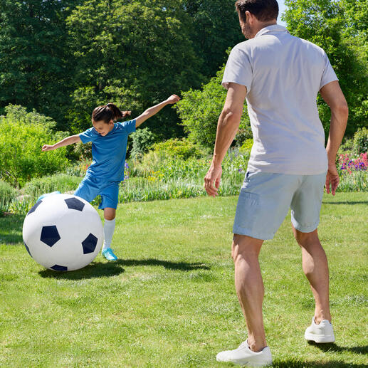 Ein Junge spielt mit einem übergroßen Fußball im Garten.
