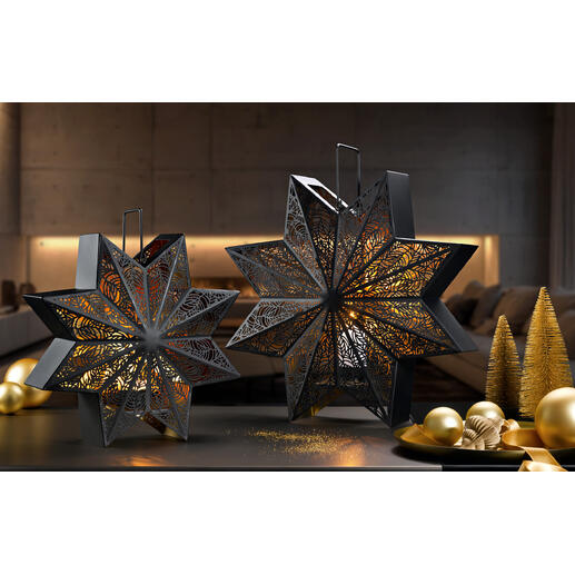 Zwei dekorative Windlichter in Sternform auf einem Tisch mit goldenen Weihnachtskugeln.
