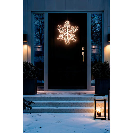 Beleuchtete LED-Schneeflocke im Außenbereich, hängend vor einer Haustüre.
