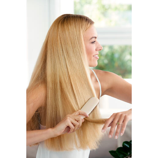 Frau mit blonden Haaren bürstet ihre Haare mit einer Haarbürste auf einem hellen Hintergrund.