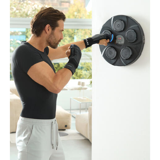 Mann schlägt mit Händen gegen Wandboxtrainer, Fitnessraum mit hellen Fenstern im Hintergrund.