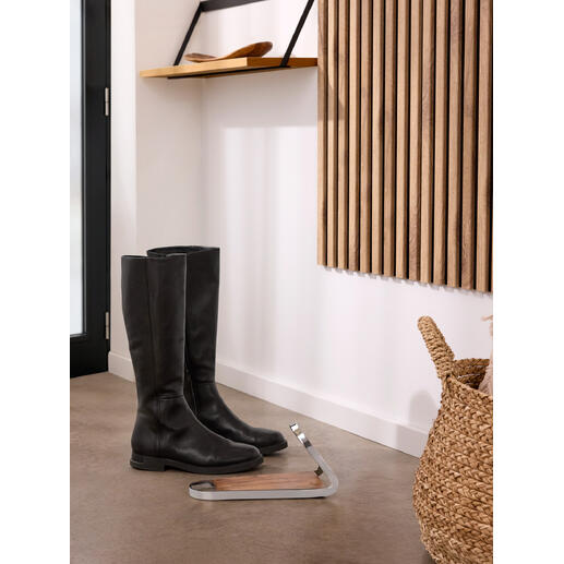 Schwarze Stiefel stehen neben einem modernen Stiefelknecht aus Holz und Metall.