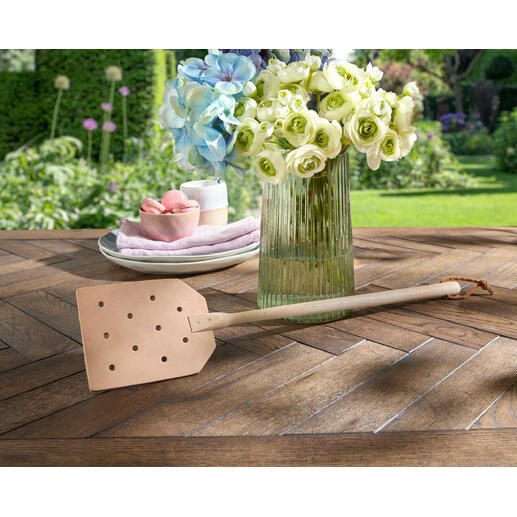 Leder-Fliegenklatsche liegt dekorativ auf einem rustikalen Holztisch.