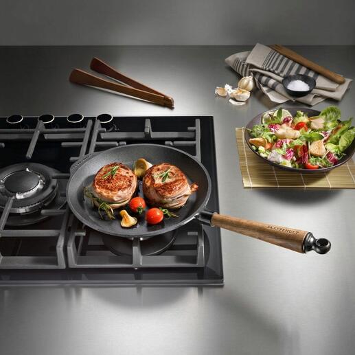 Gusseisenpfanne auf Kochfeld mit gebratenem Fleisch und Gemüse