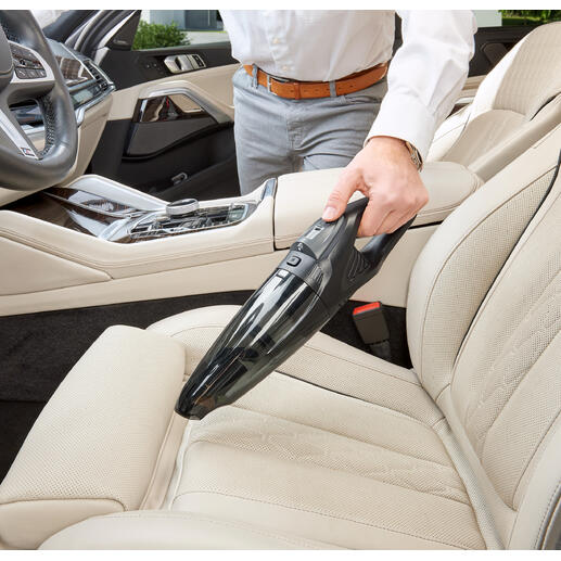 Mann benutzt einen Akku-Handsauger zur Reinigung des Autositzes mit hellem Interieur.