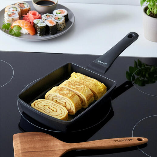 Tamagoyaki-Pfanne mit gefalteten Eiern neben Sushi-Platte.