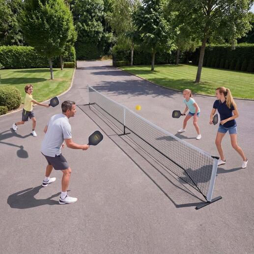 Familie spielt Pickleball im Freien, mit Netz und Bällen.