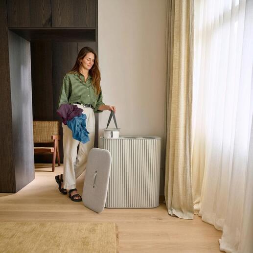 Frau mit bunten Kleidungsstücken steht neben einem Wäschesammler.
