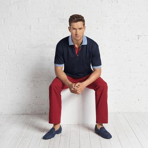Mann sitzt auf einem Kasten, trägt ein dunkelblaues Polo und rote Hose.