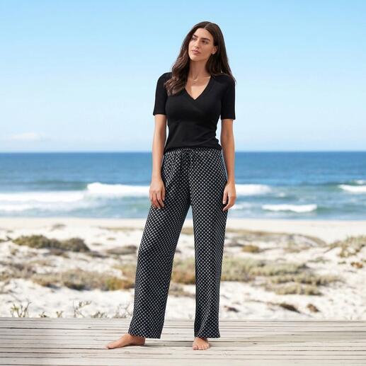 Frau in schwarzem Wickel-Shirt und gemusterter Hose am Strand