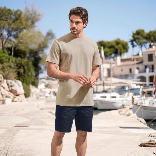 Mann im beigen T-Shirt und blauen Shorts steht am Hafen.