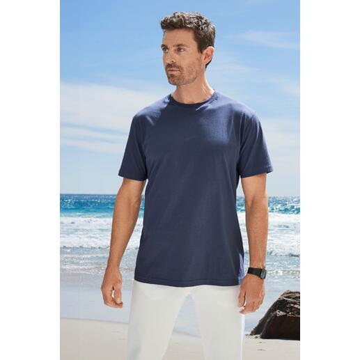 Mann in dunkelblauem T-Shirt steht am Strand mit Blick zur Kamera.