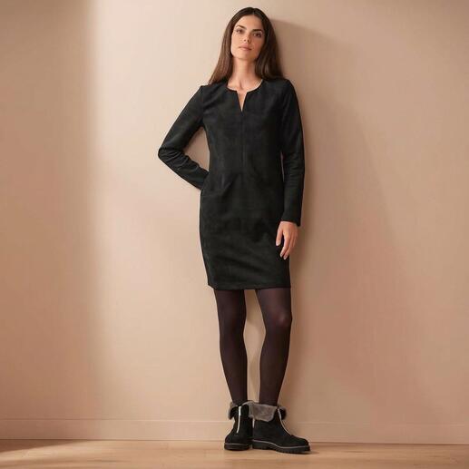 Frau in schwarzem Alcantara®-Kleid mit langen Ärmeln, an der Wand stehend.