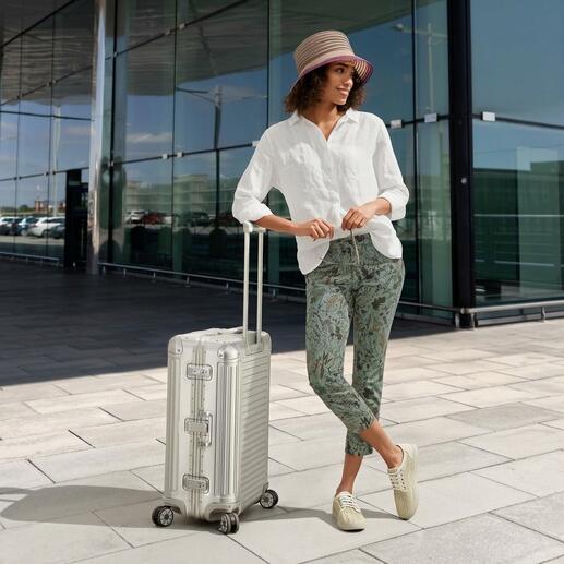 Frau in einer weißen Leinen-Tunika steht am Flughafen neben einem Koffer.