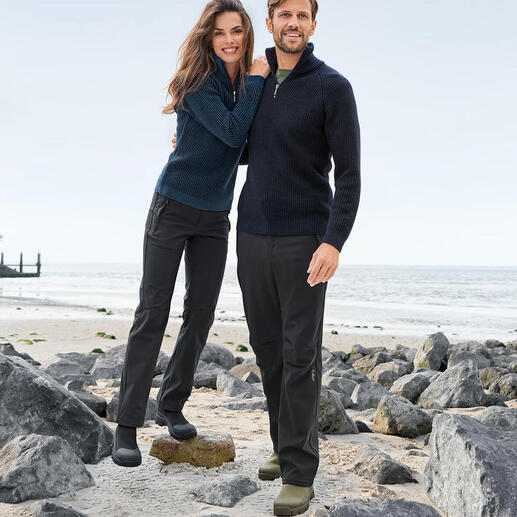 Paar in Seemannstroyern am Strand, umgeben von Steinen und Meer.