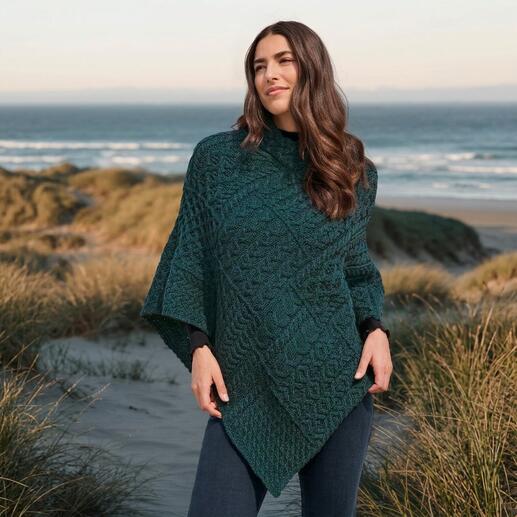 Frau im Aran-Poncho posiert am Strand.