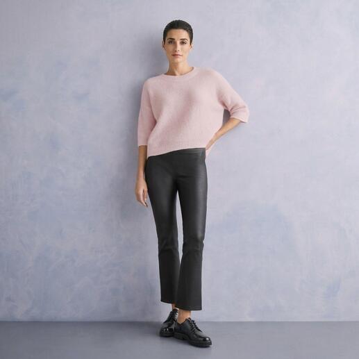 Frau in pinkem Sweater und schwarzer Kick-Flare-Lederhose vor grauem Hintergrund.