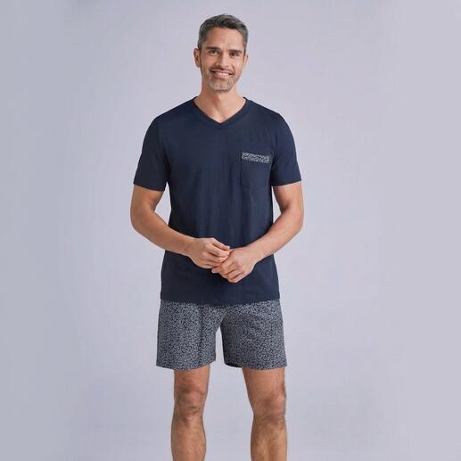 Mann in navy-blauem T-Shirt und grauen Shorts, lächelt vor neutralem Hintergrund.
