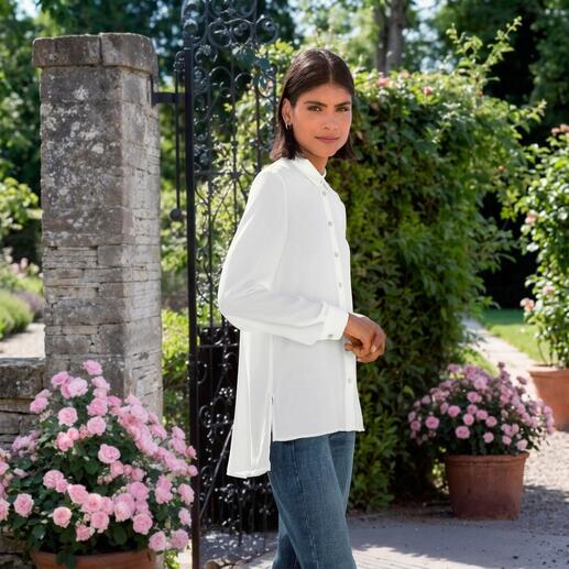 Frau in weißer High-Low-Bluse steht draußen mit Blumen