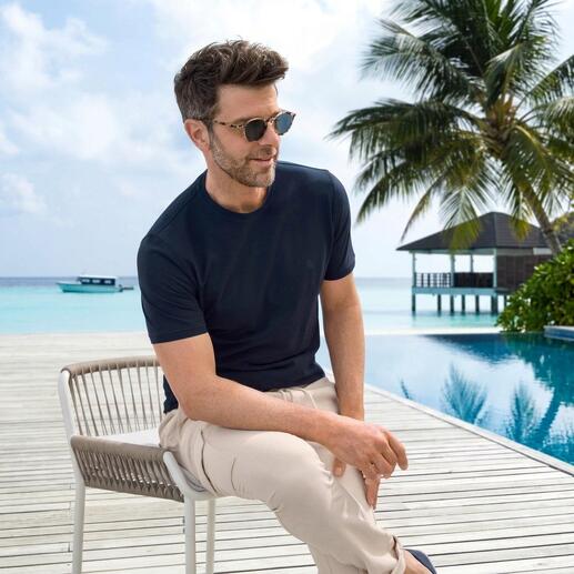 Mann in dunkelblauem T-Shirt mit Sonnenbrille, sitzt am Pool.
