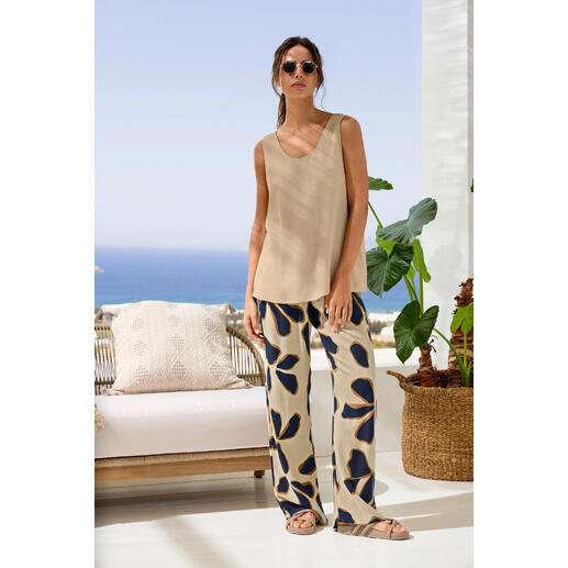 Top und Hose Frau in beigem Top und gemusterter Hose auf einer Terrasse, frontal.